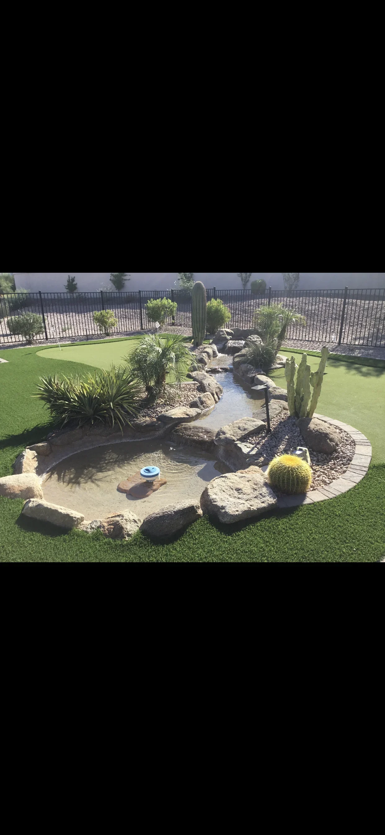 Desert garden with synthetic turf, central water feature, cacti, and boulder landscaping