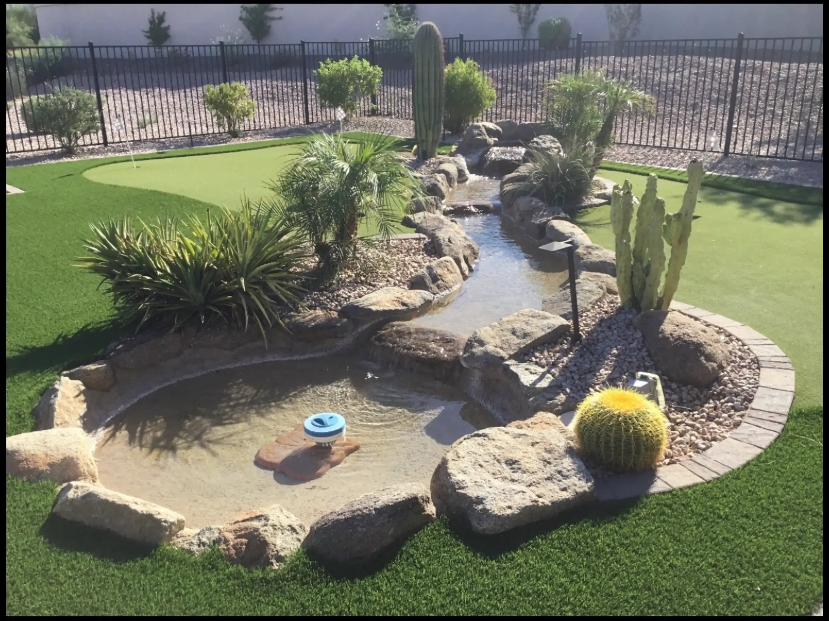 Synthetic putting green with desert plants, water feature, and stone accents in backyard
